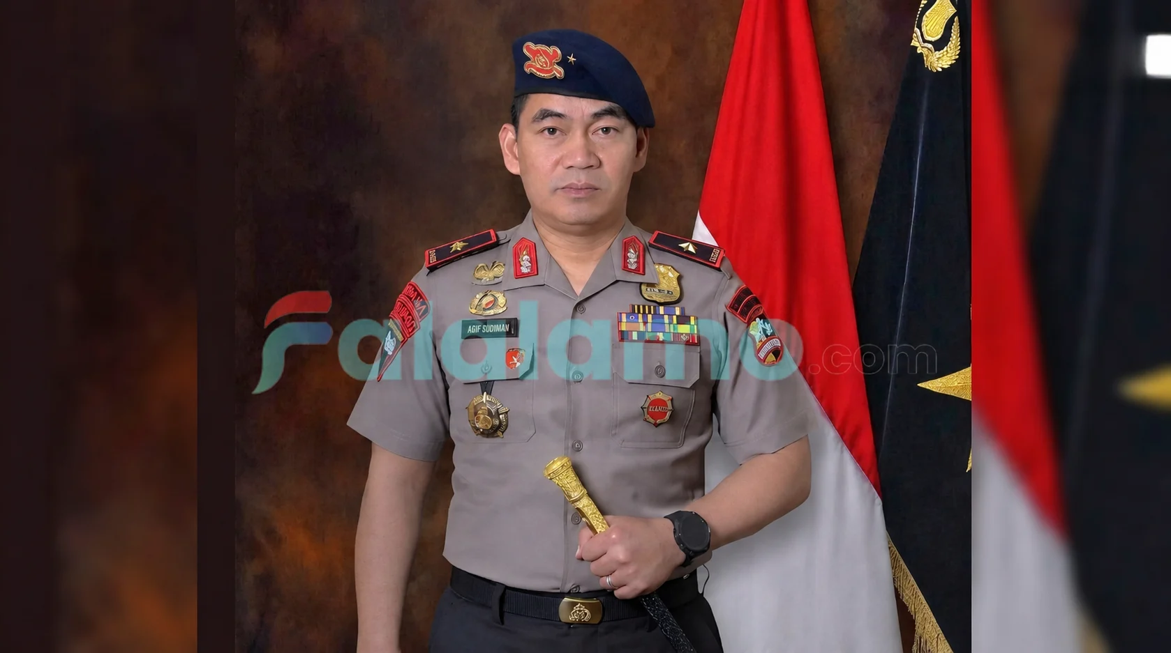 Potret resmi Brigjen Pol. Arif Budiman, S.I.K., M.H. dalam seragam dinas lengkap kepolisian, memegang tongkat komando dengan latar belakang bendera Merah Putih.